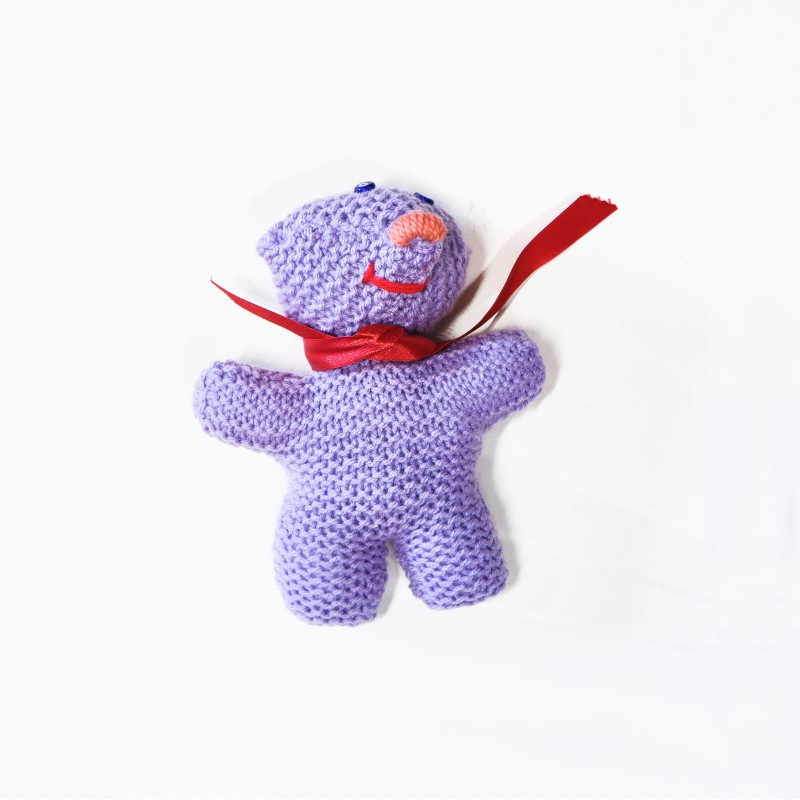 Purple knitted smiling doll with a red ribbon around the neck